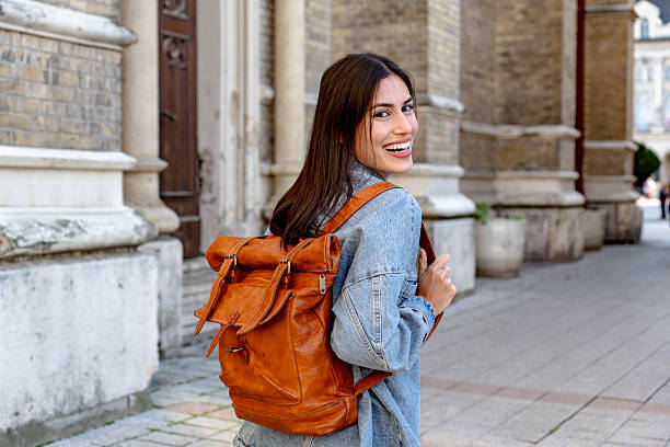 Happy young woman with a backpack walking near a church in a european city and looking at the camera