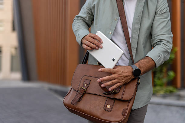 Businessman walking outdoors, placing a samsung tablet into a stylish leather bag